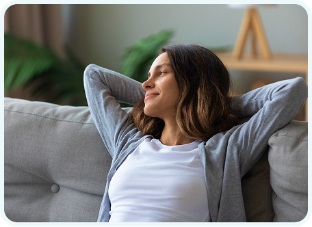 Woman relaxing on a couch with her hands behind her head, looking content and at ease.