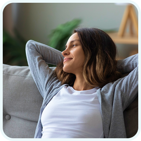 Woman relaxing on a couch with her hands behind her head, looking content and at ease.