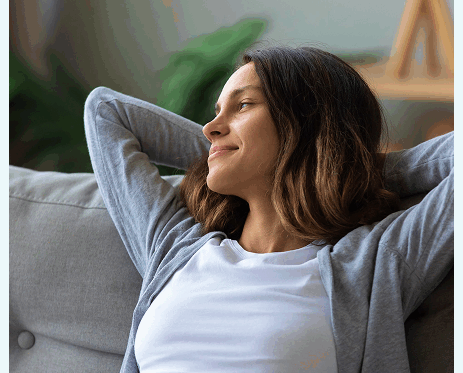 Woman relaxing on a couch with her hands behind her head, looking content and at ease.