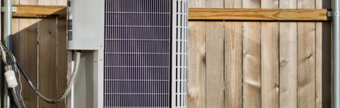 Central air conditioning unit in a residential backyard in front of a wooden fence