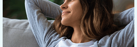 Woman relaxing on a couch with her hands behind her head, looking content and at ease.