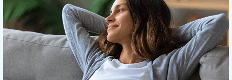 Woman relaxing on a couch with her hands behind her head, looking content and at ease.