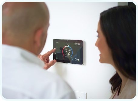 Two people looking at and adjusting a smart thermostat mounted on the wall.